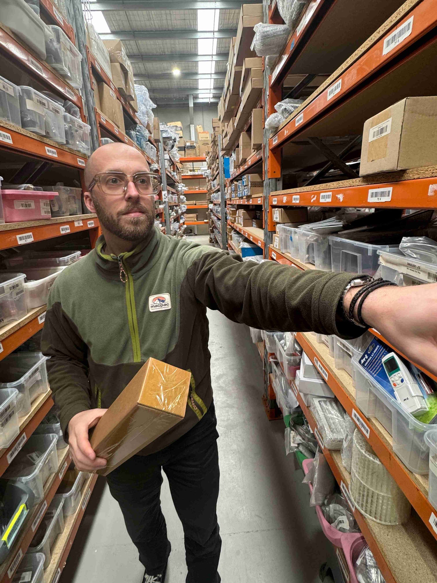 Person holding a box in a warehouse setting with shelves and boxes in the background
